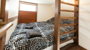 A small, single-bed room with a wooden headboard, a window, and a wooden ladder. - Nozawa Cottage (Nozawaonsen)