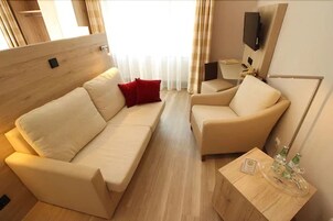 Una habitación acogedora con sofá y sillón, una mesita con artículos de aseo, y un televisor montado en la pared.