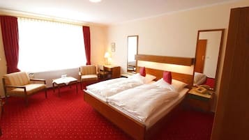 A hotel room with a large bed, two bedside tables, a chair, a small table, a lamp, and a mirror.