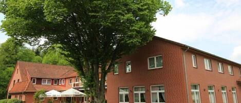 Un bâtiment en briques rouges, doté de nombreuses fenêtres et d’un grand arbre devant.