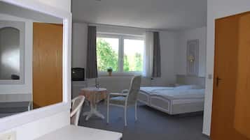 A hotel room with a bed, a desk, and a chair. There is a window with curtains and a view of greenery outside.