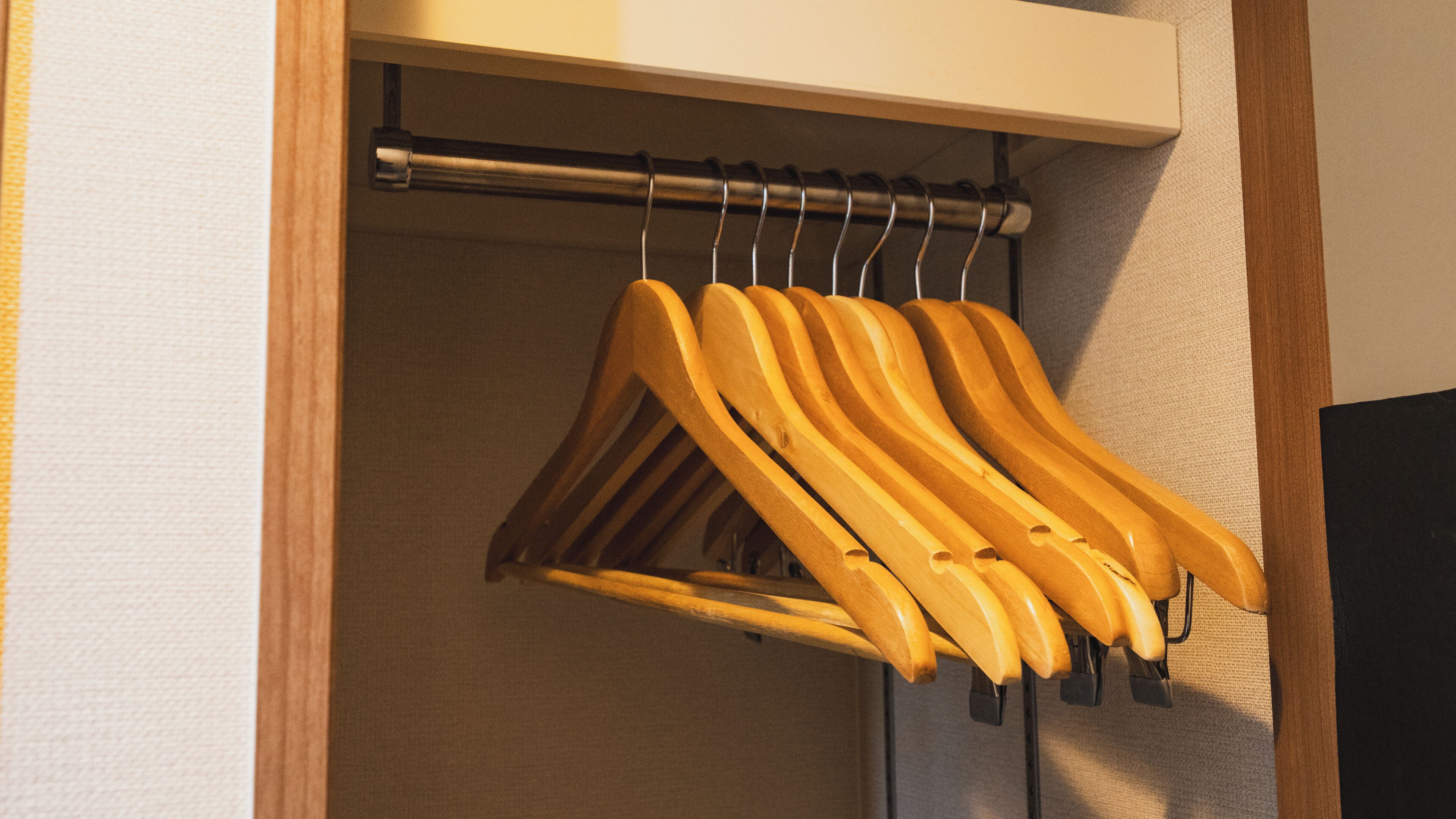 A closet with wooden hangers hanging on a metal rod.