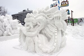 A snow sculpture of a dragon with intricate details, set against a backdrop of a building and a colorful sign. - The Base Sapporo Susukino (Sapporo)