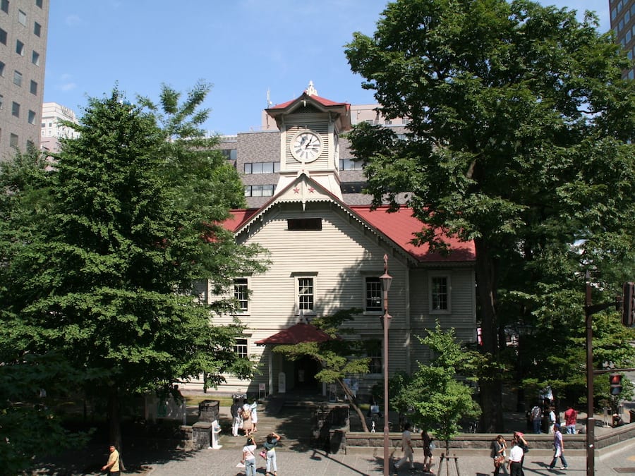 Un edificio histórico con una torre de reloj, rodeado de árboles y edificios modernos.