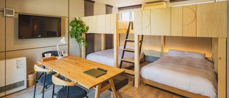 Habitación pequeña con literas, escritorio, sillas, televisor y una planta.