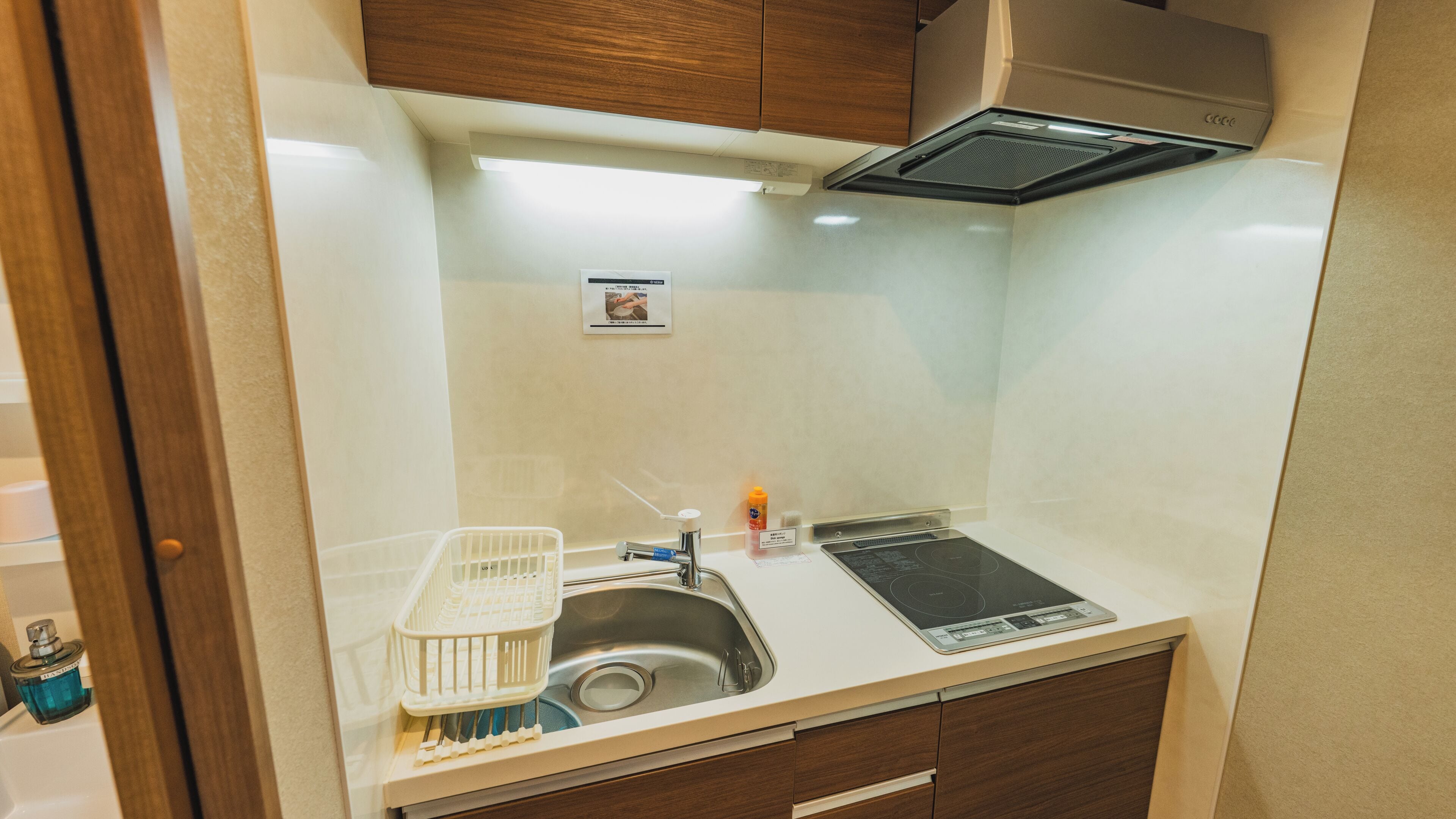 A compact kitchenette with a sink, a dish rack, a bottle, and a stove.