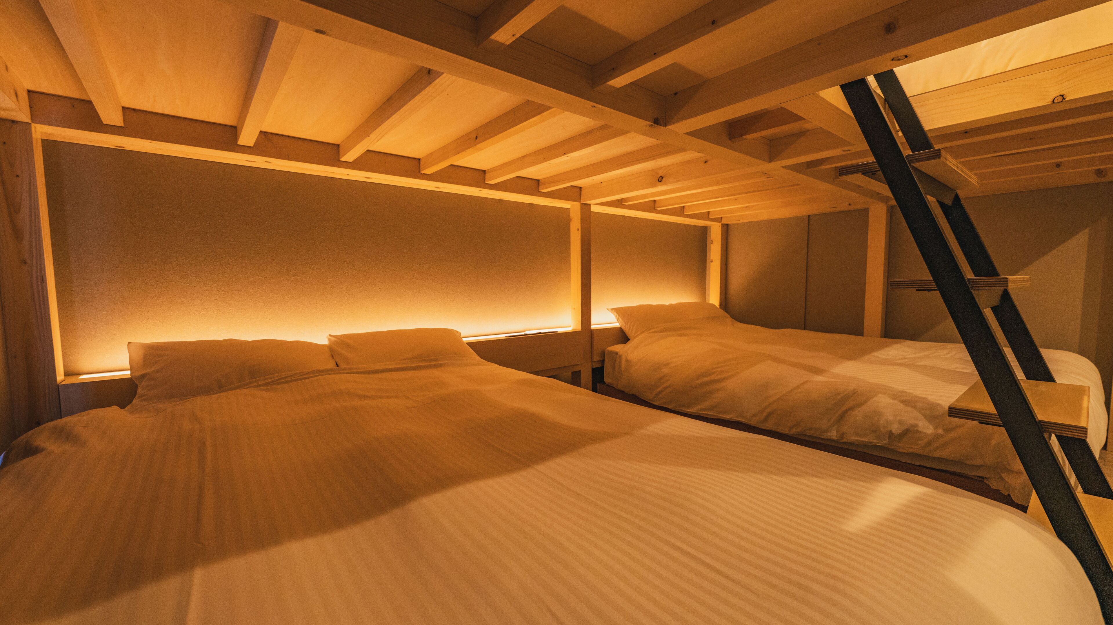 Une chambre avec deux lits, des poutres en bois et une échelle.