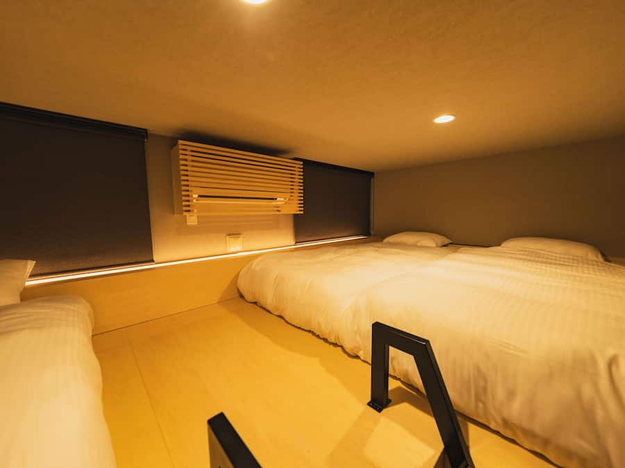 Una habitación de hotel con cama, mesita de noche, aire acondicionado de pared y luz en el techo.