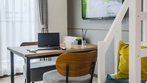 Una habitación moderna con un escritorio de madera, una computadora portátil, una taza blanca, una planta pequeña y un televisor en la pared.