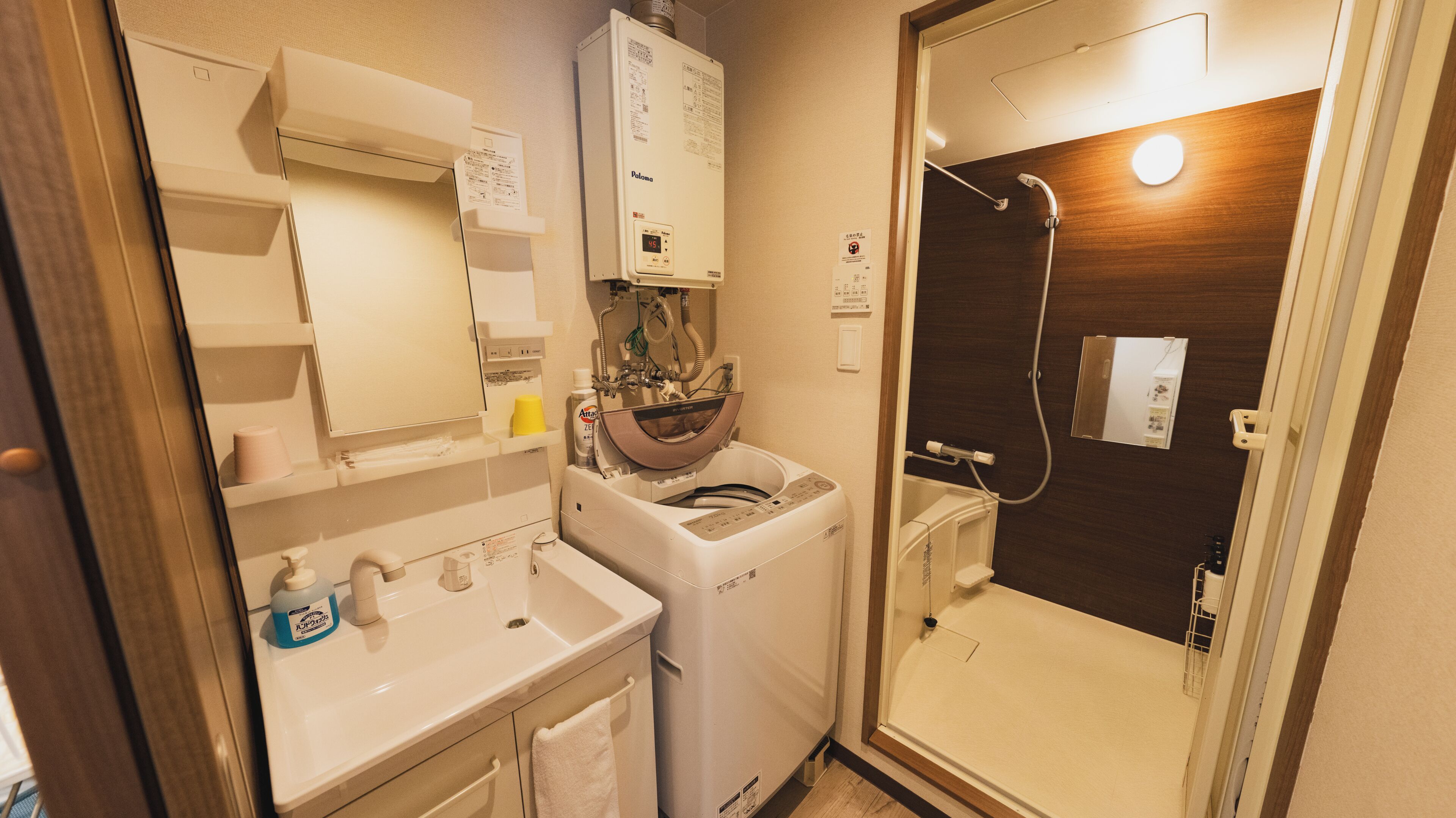 A compact bathroom with a washing machine, a sink, and a shower.