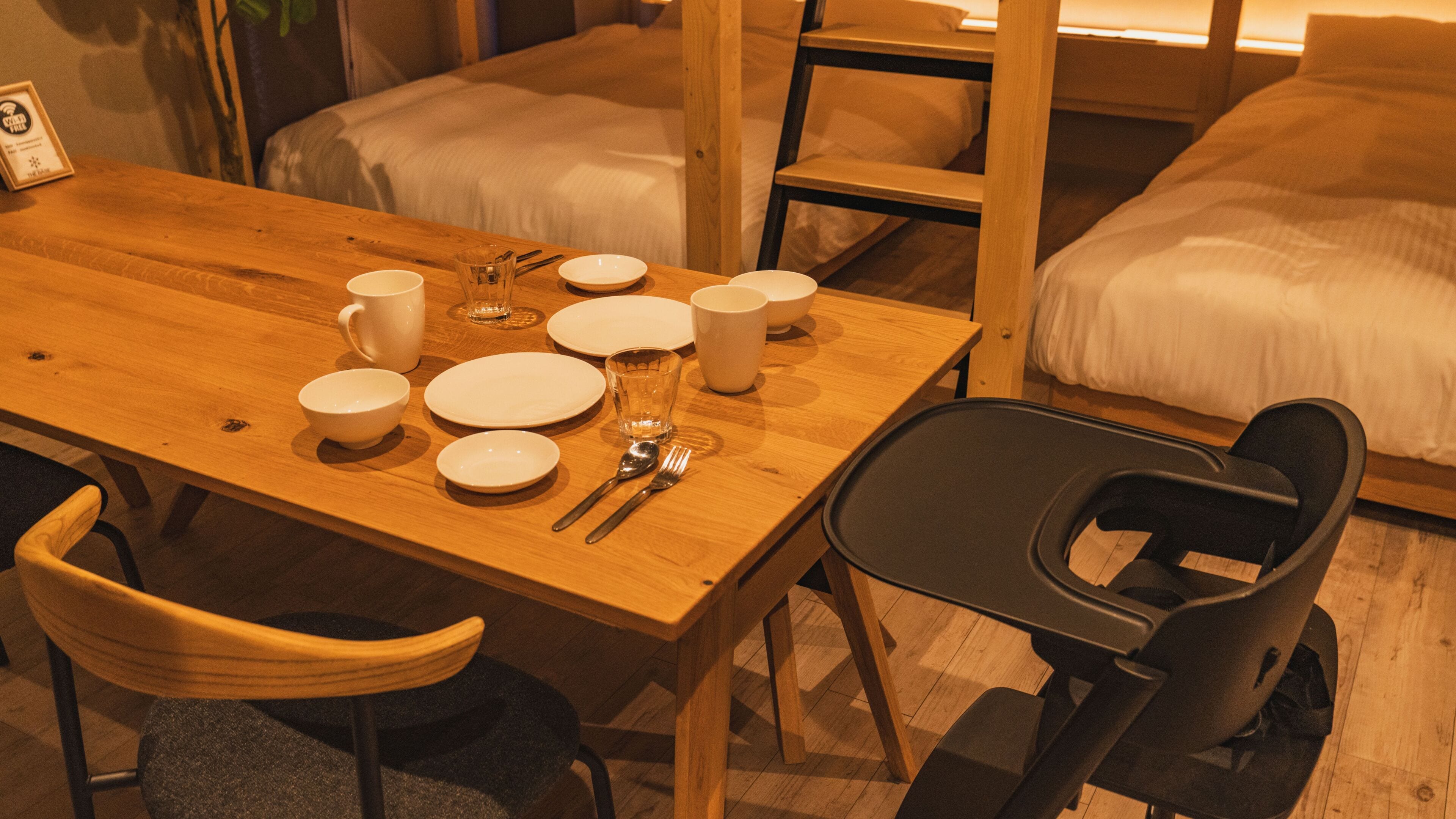 A wooden dining table set with white plates, bowls, glasses, cutlery, and a black chair.