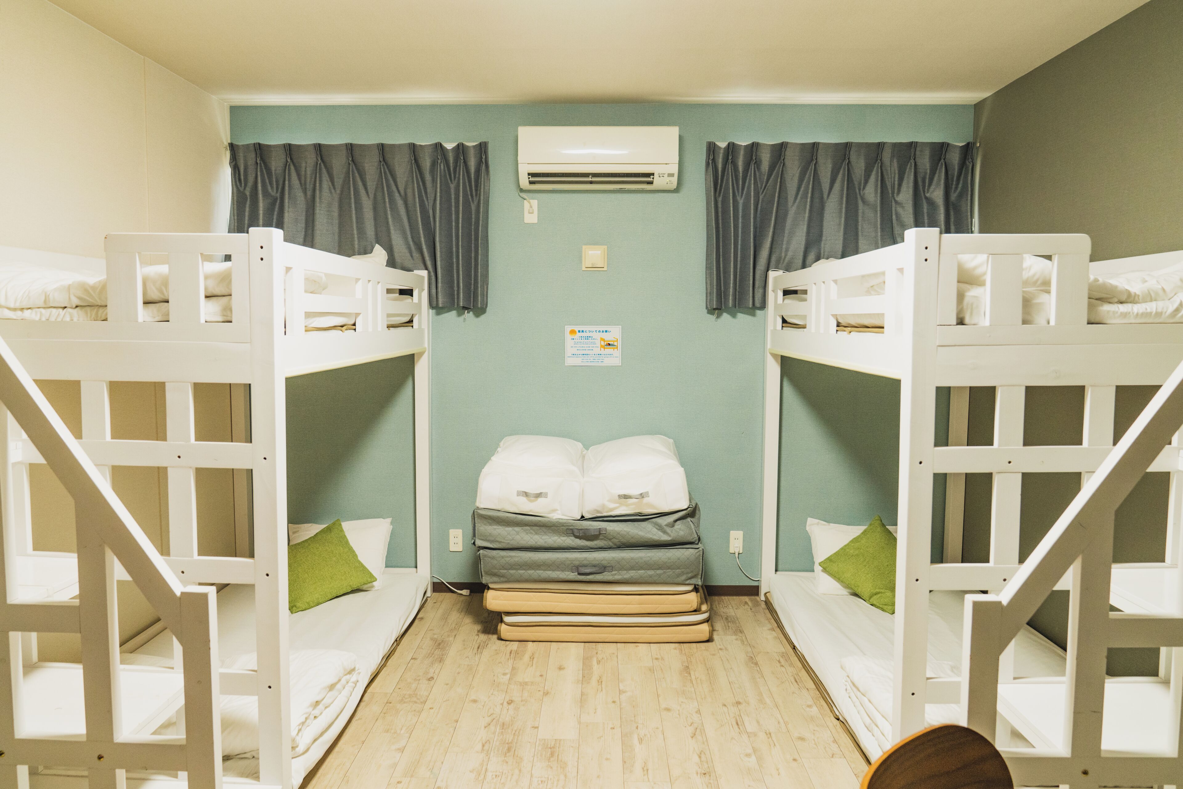 A room with bunk beds, a single bed, a wall-mounted air conditioner, and a small sign on the wall.