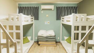 A room with bunk beds, a single bed, a wall-mounted air conditioner, and a small sign on the wall.