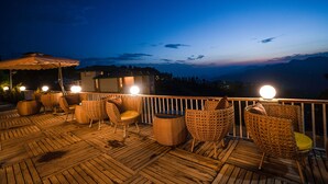 A wooden deck with wicker furniture and a view of the mountains at dusk. - The Alpine Chalet Resort (Dhari)