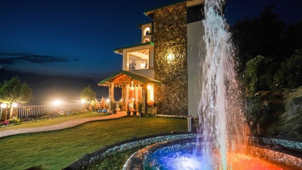 A building with a stone facade, a fountain, and a well-maintained garden at night. - The Alpine Chalet Resort (Dhari)