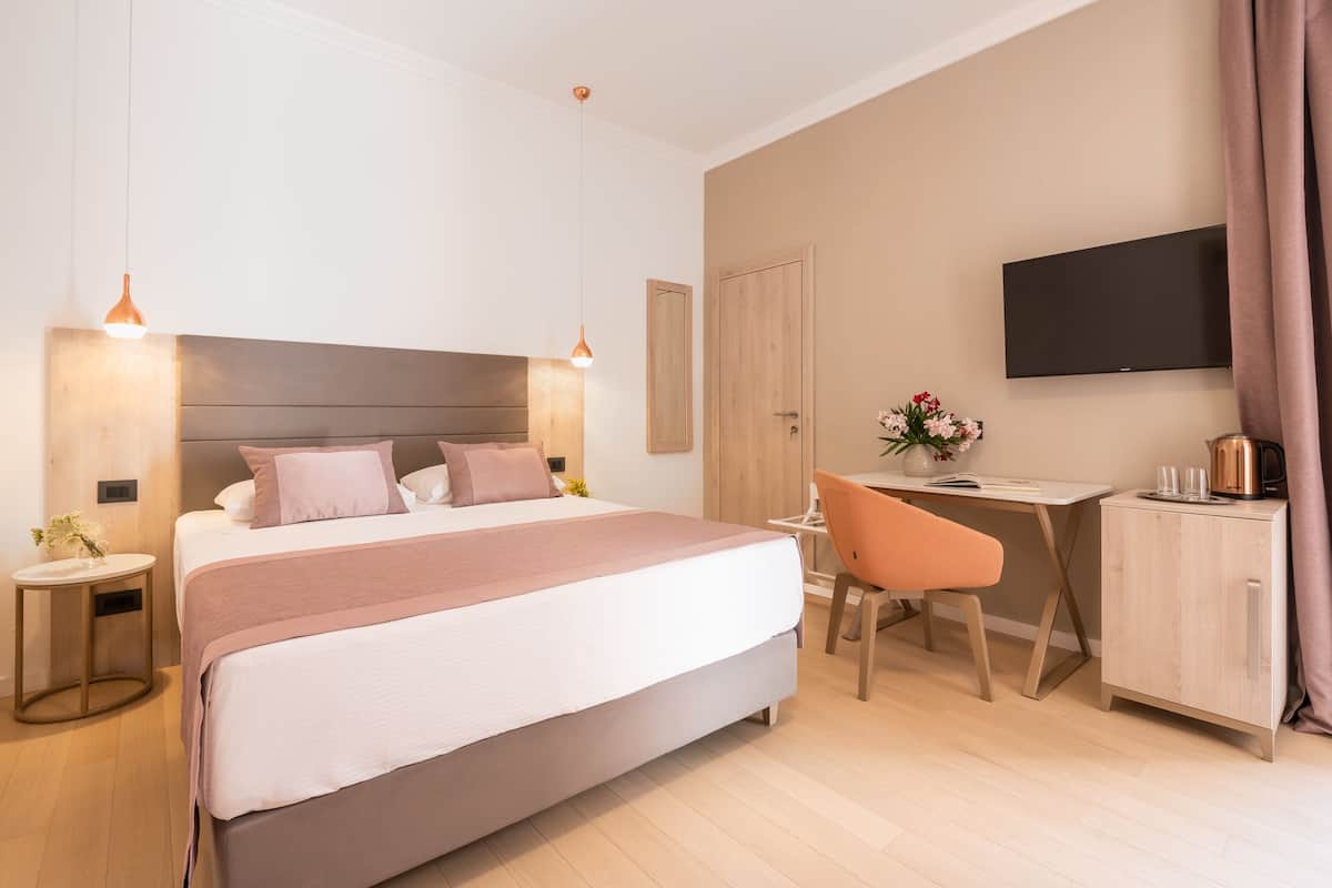 A modern hotel room with a large bed, bedside tables, a desk, and a flat-screen TV.