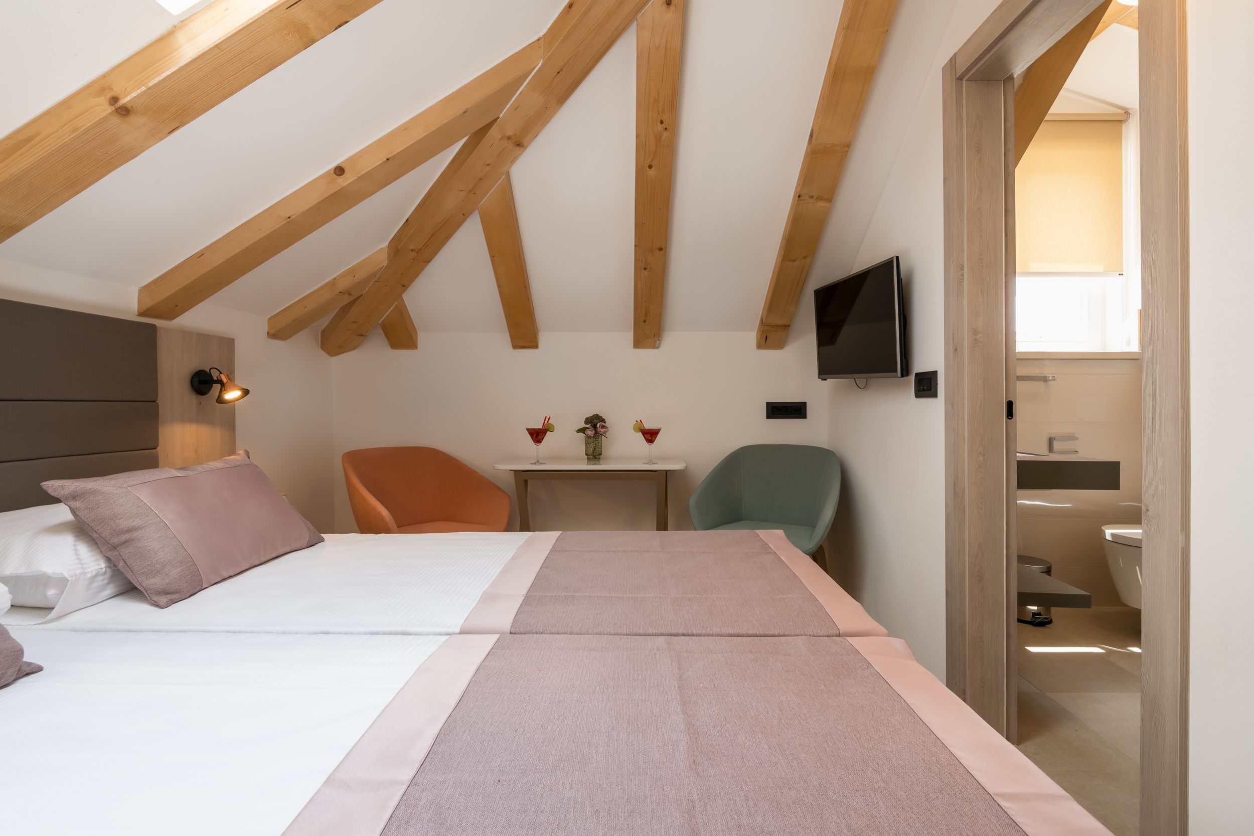 Een slaapkamer met een bed, een bureau, een stoel, een televisie en een zichtbare badkamer door een geopende deur.