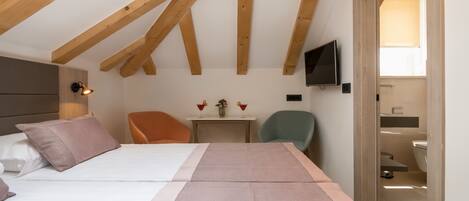 A bedroom with a bed, a desk, a chair, a television, and a bathroom visible through an open door.