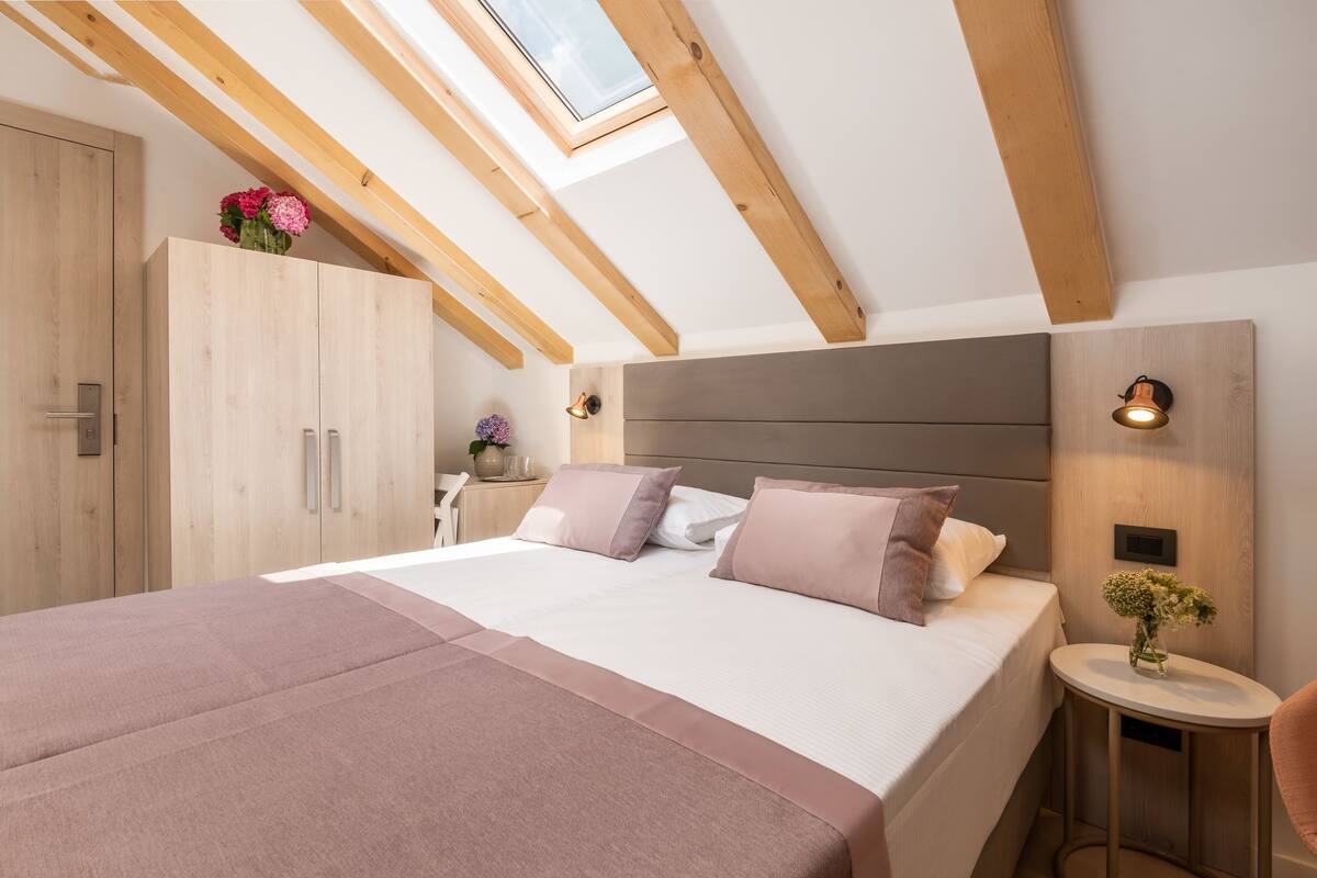A bedroom with a skylight, wooden beams, a bed with a headboard, bedside tables, and a wardrobe.