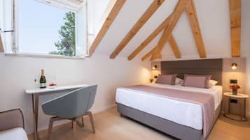 A bedroom with a large bed, a desk, and a chair. There is a window with a view of trees outside.