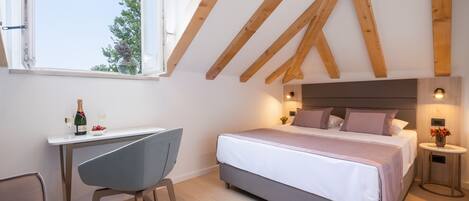 A bedroom with a large bed, a desk, and a chair. There is a window with a view of trees outside.