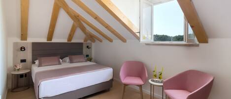 A bedroom with a bed, two pink chairs, a small table, and a window with a view.