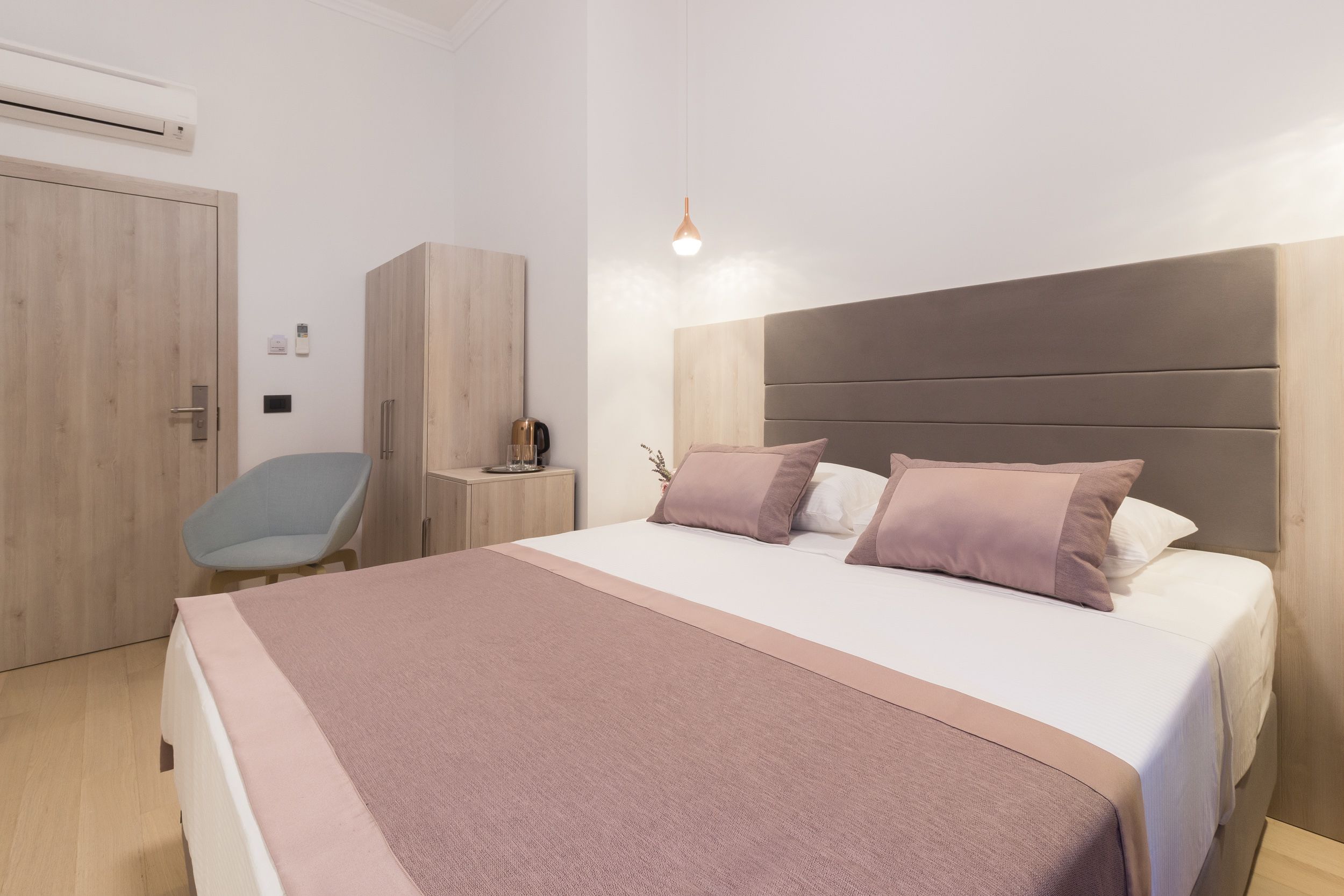 A modern bedroom with a large bed, a bedside table, a wardrobe, and a hanging light fixture.