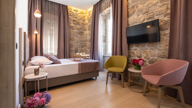 A bedroom with a bed, a TV mounted on a stone wall, a small table with flowers, and a chair.