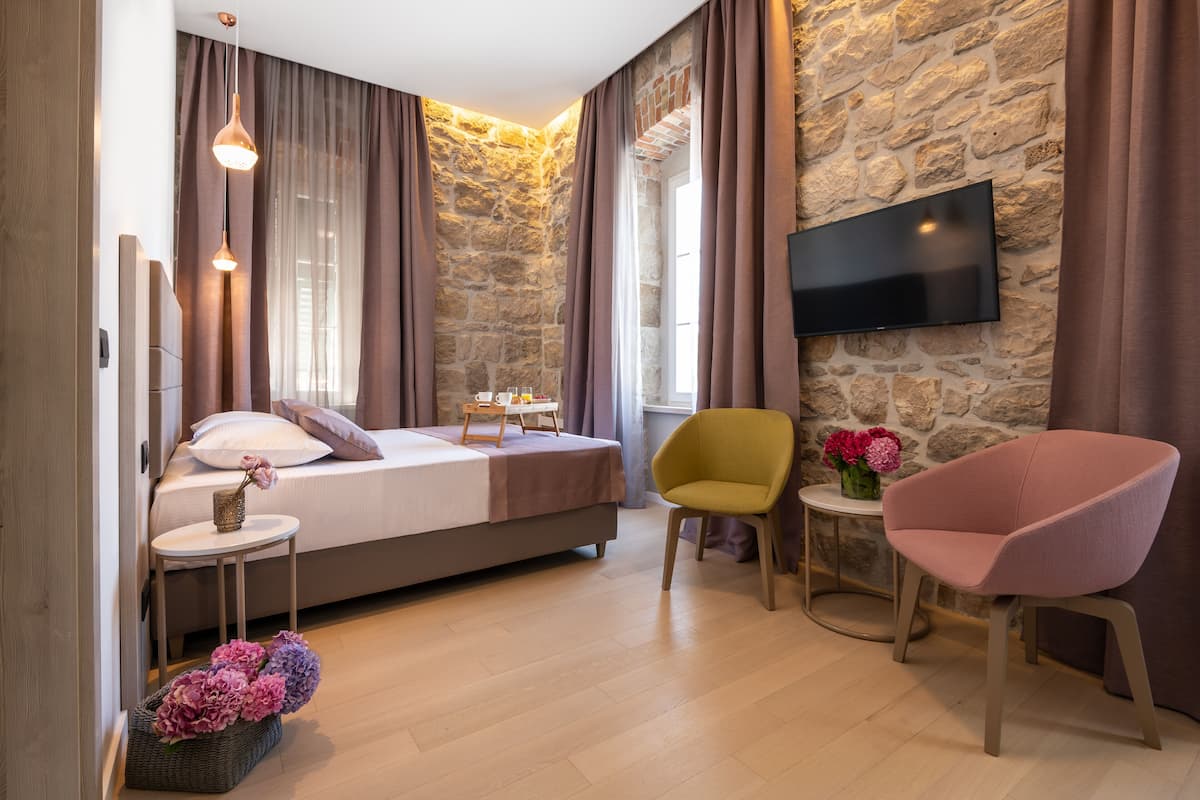 A bedroom with a bed, a TV mounted on a stone wall, a small table with flowers, and a chair.