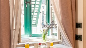 A small table with a yellow chair, a window with green shutters, and a vase with flowers.