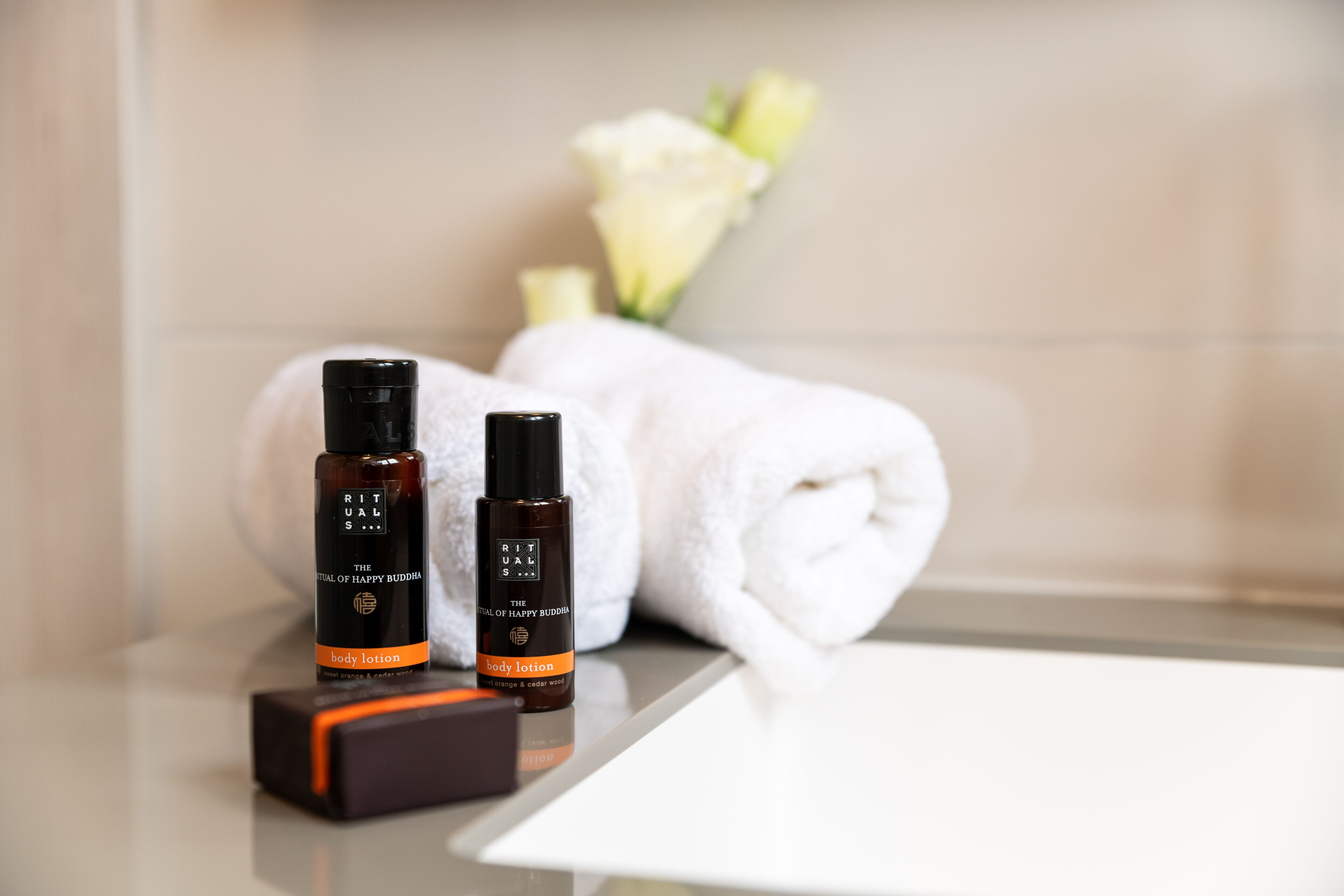 A bathroom with a white towel, two bottles of body lotion, and a small box.