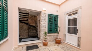 A stone-floored entrance with a staircase, green shutters, and a door marked with the number 6.