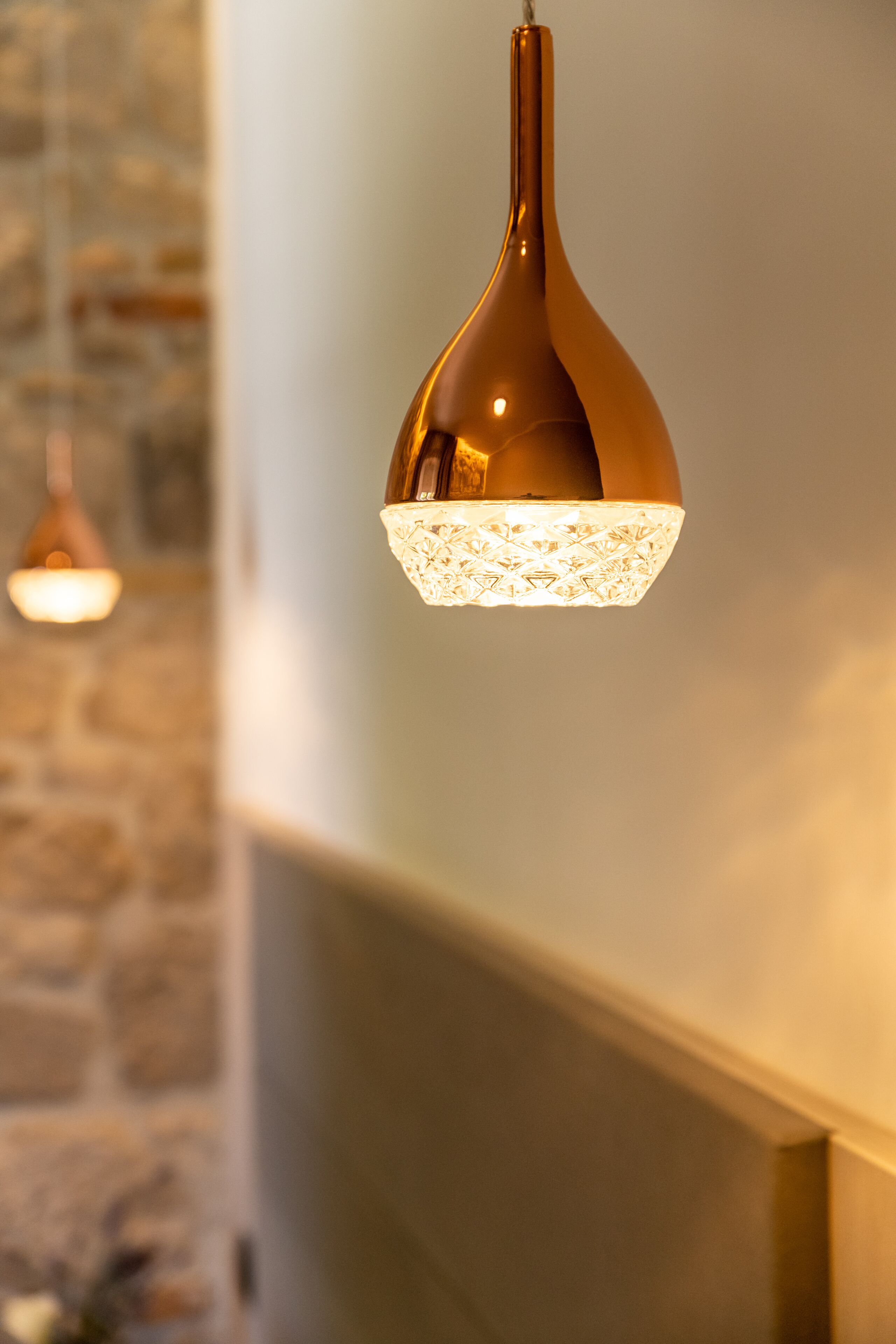 Una lámpara colgante con pantalla de vidrio texturizado y base metálica, suspendida del techo en una habitación con pared de piedra.