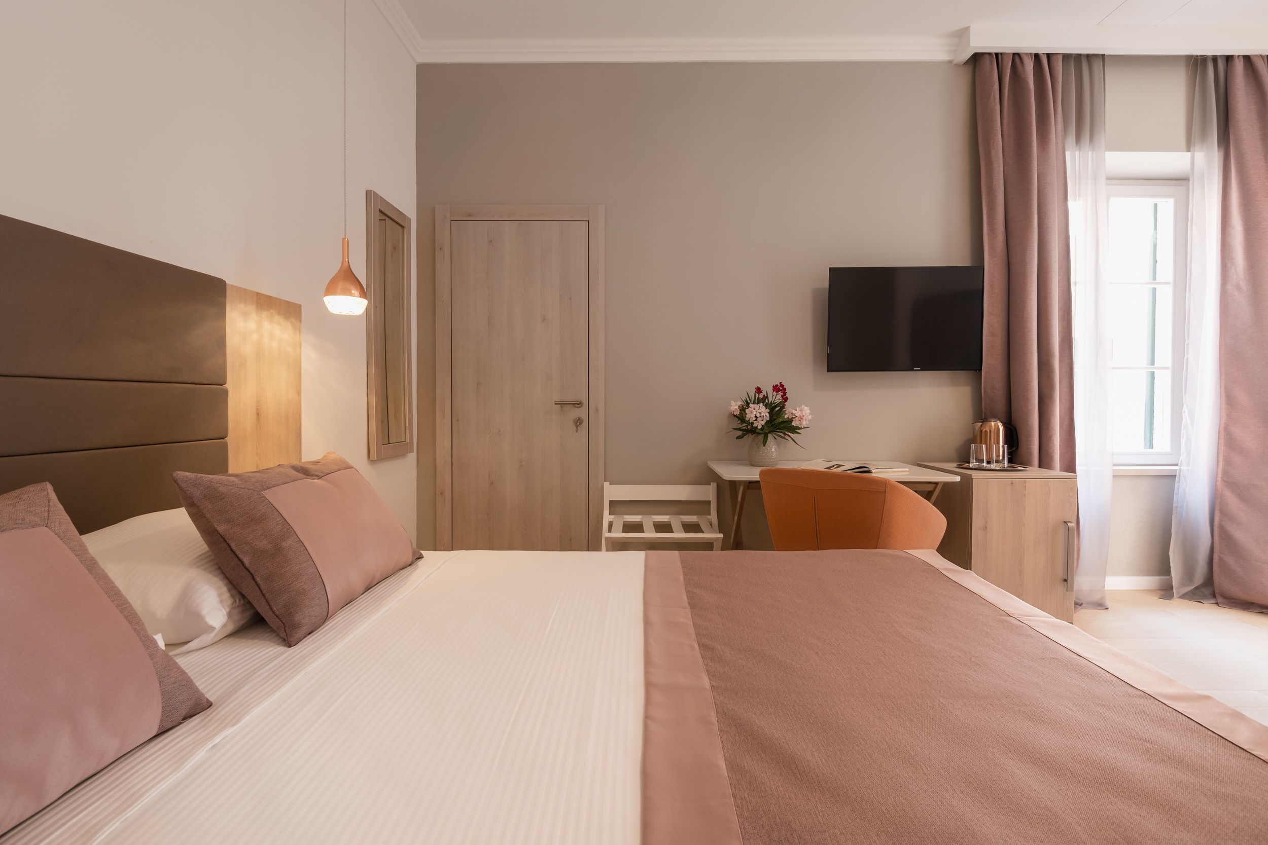 Habitación de hotel con una cama grande, un escritorio, una silla, un televisor y una ventana con cortinas.