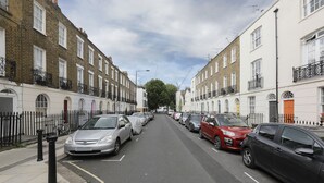 A street lined with terraced houses, parked cars, and a clear sky. - Cozy Apartment in Camden Town (London)