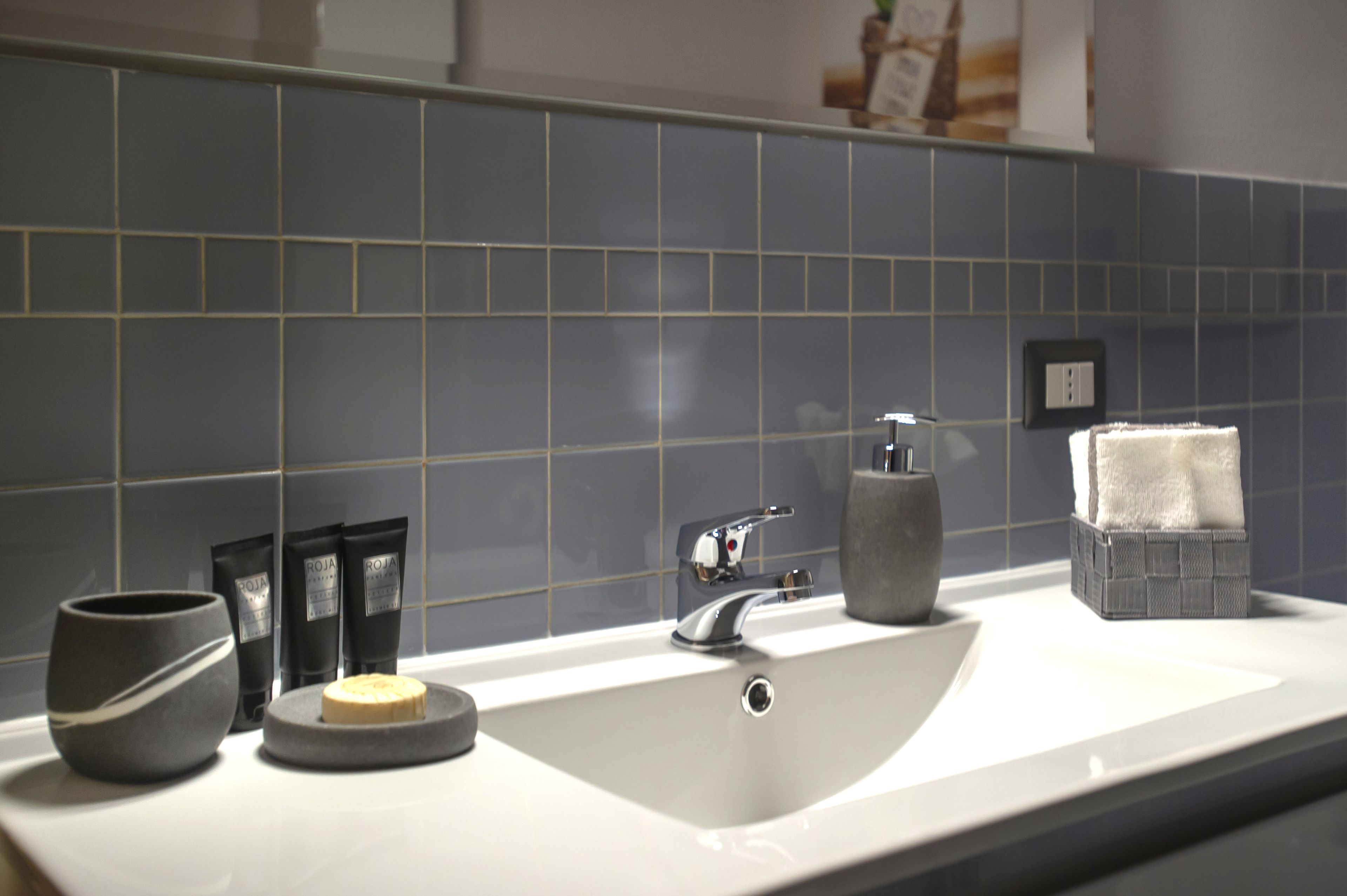 Ein Badezimmer mit einem weißen Waschbecken, dunkelblauen Fliesen, einer Seifenschale und Pflegeprodukten.