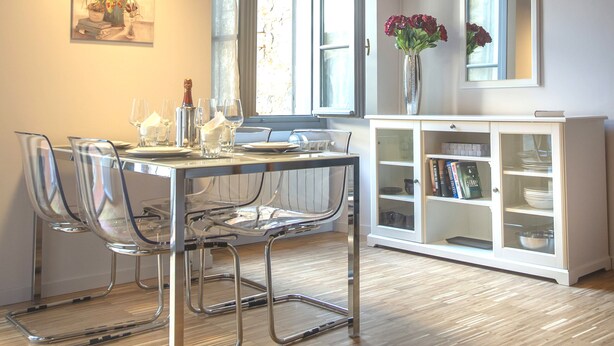 Un comedor con techo de madera, luces colgantes, una mesa de comedor con sillas, un jarrón con flores y un armario con estantes.