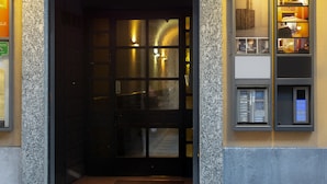 Entrada de hotel con arco de piedra, puerta numerada y un pequeño escaparate a la derecha.
