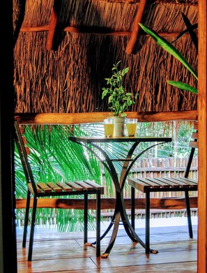 Een houten tafel met twee stoelen onder een rieten dak, met uitzicht op het groene gebladerte.