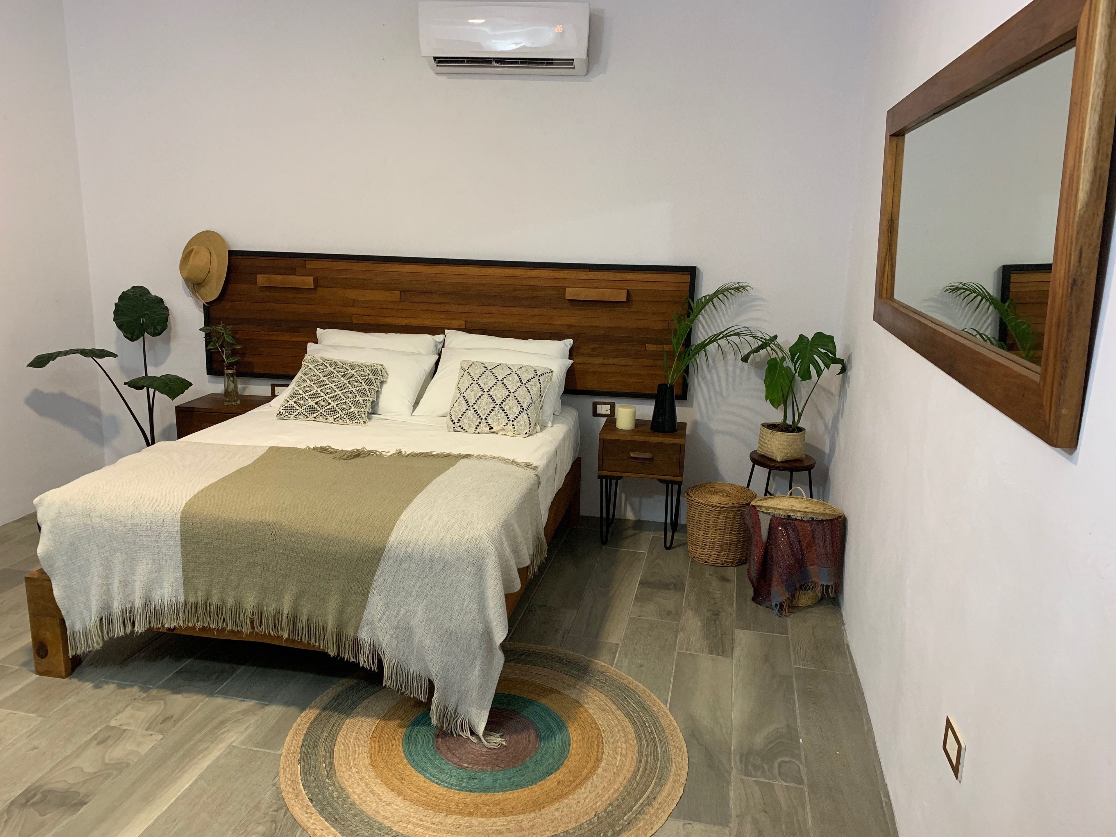 Un dormitorio ordenado con cabecera de madera, una cama con almohadas estampadas, una mesita de noche con una vela y un espejo en la pared.