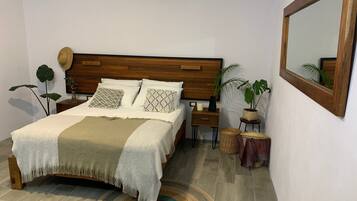 Un dormitorio ordenado con cabecera de madera, una cama con almohadas estampadas, una mesita de noche con una vela y un espejo en la pared.