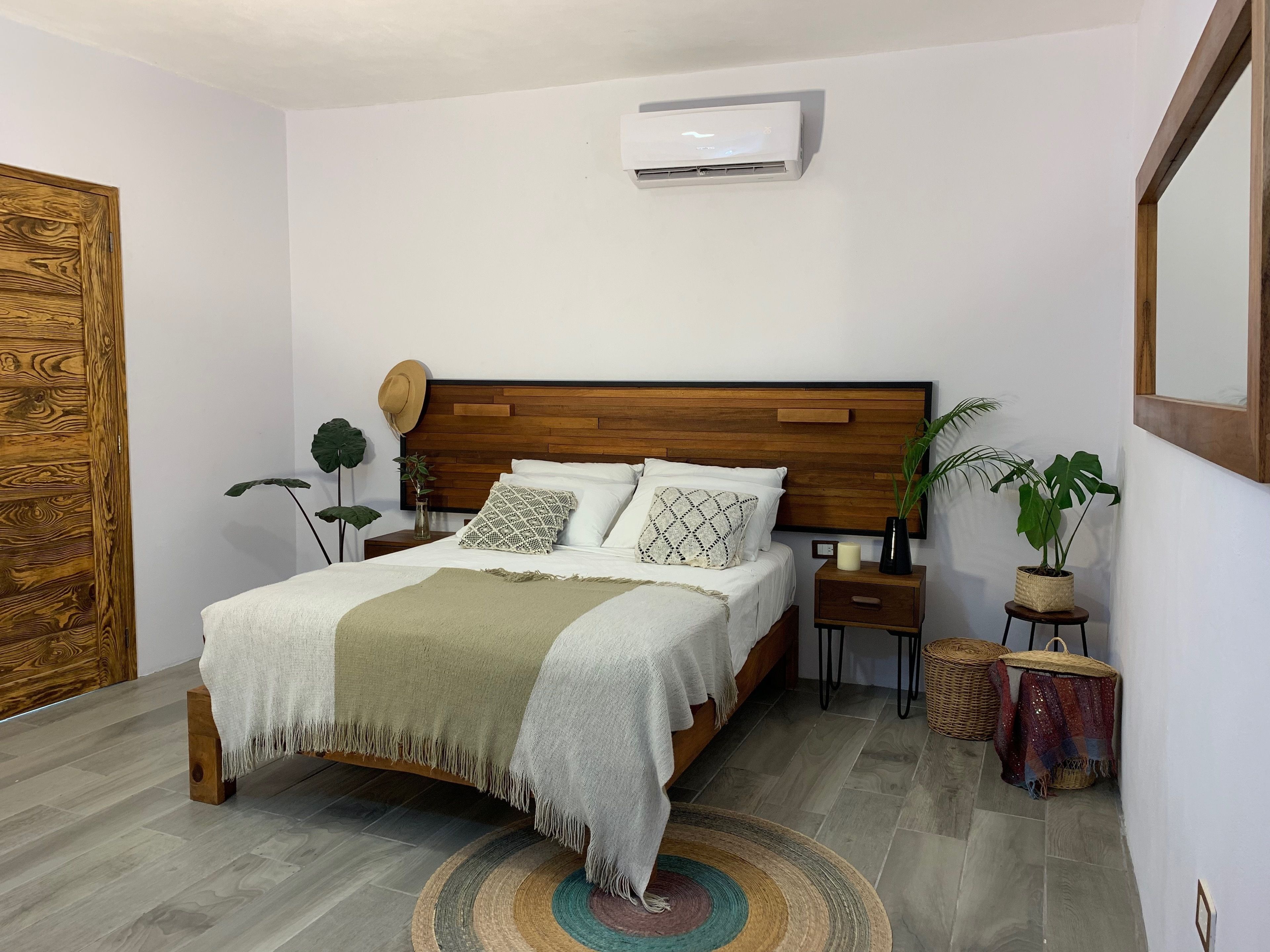A neatly arranged bedroom with a wooden bed, a bedside table, a nightstand, a potted plant, and a mirror on the wall.