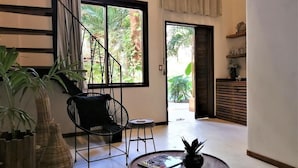 A modern living room with a large window, a black chair, a small table, and a potted plant. - Hotel Boutique TerraNova (Tulum)