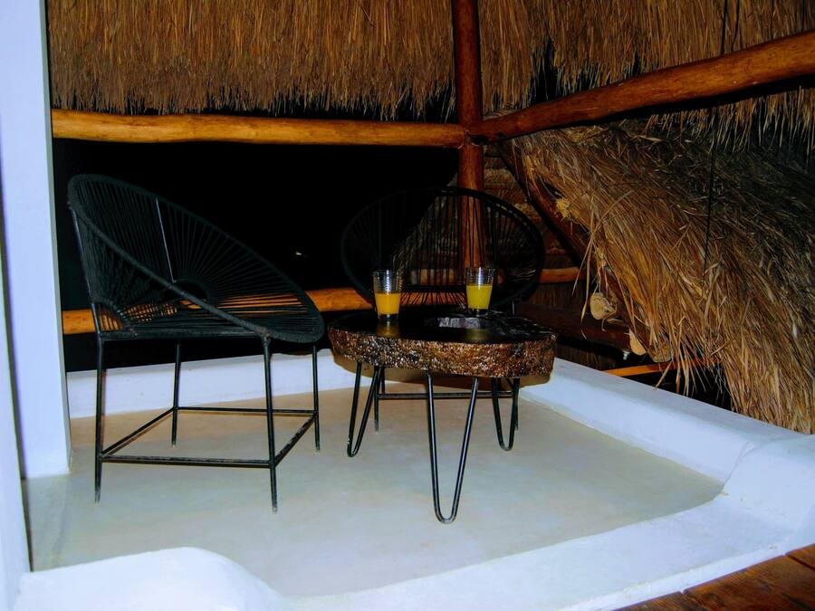 A thatched-roof outdoor seating area with two chairs and a table, likely used for dining or socializing.