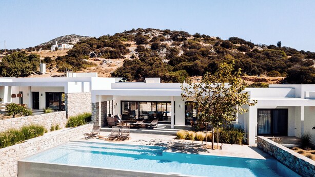 A modern villa with a swimming pool, outdoor seating, and a view of a hillside. - Hidden Hill Villas (Naxos)