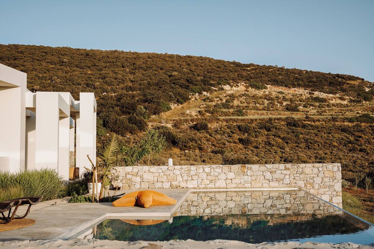 A modern pool area with stone walls and a view of a hilly landscape.