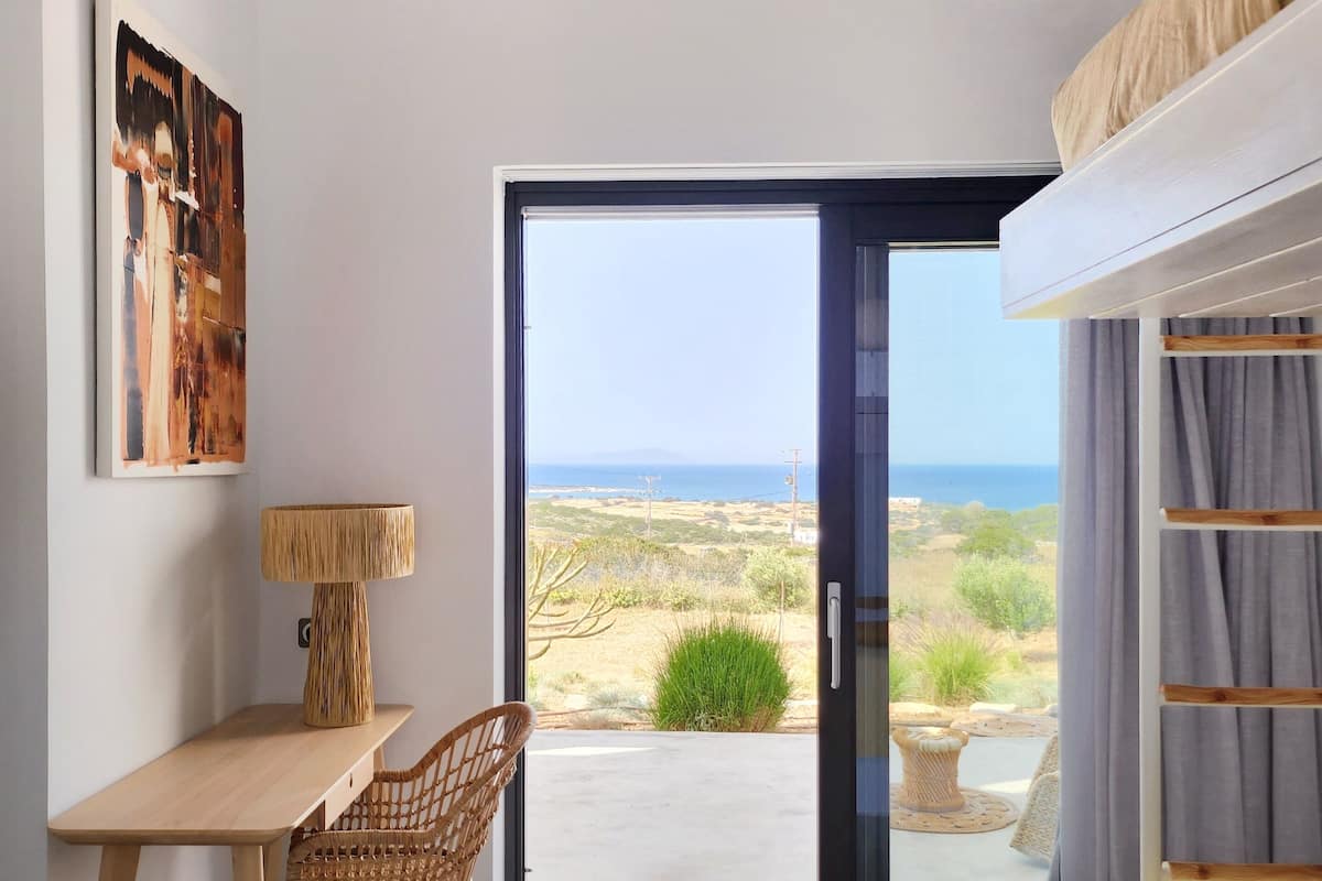A room with a bed, a desk, a chair, and a view of the outdoors.