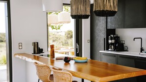 A modern kitchen with a wooden table, wicker chairs, and a coffee machine. - Hidden Hill Villas (Naxos)