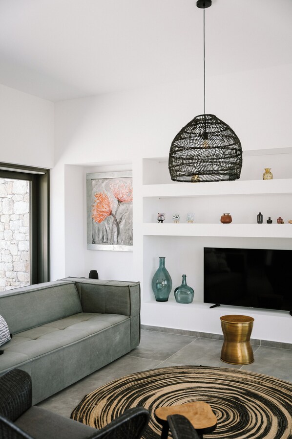 A modern living room with a grey sofa, a black TV, and decorative items on shelves.