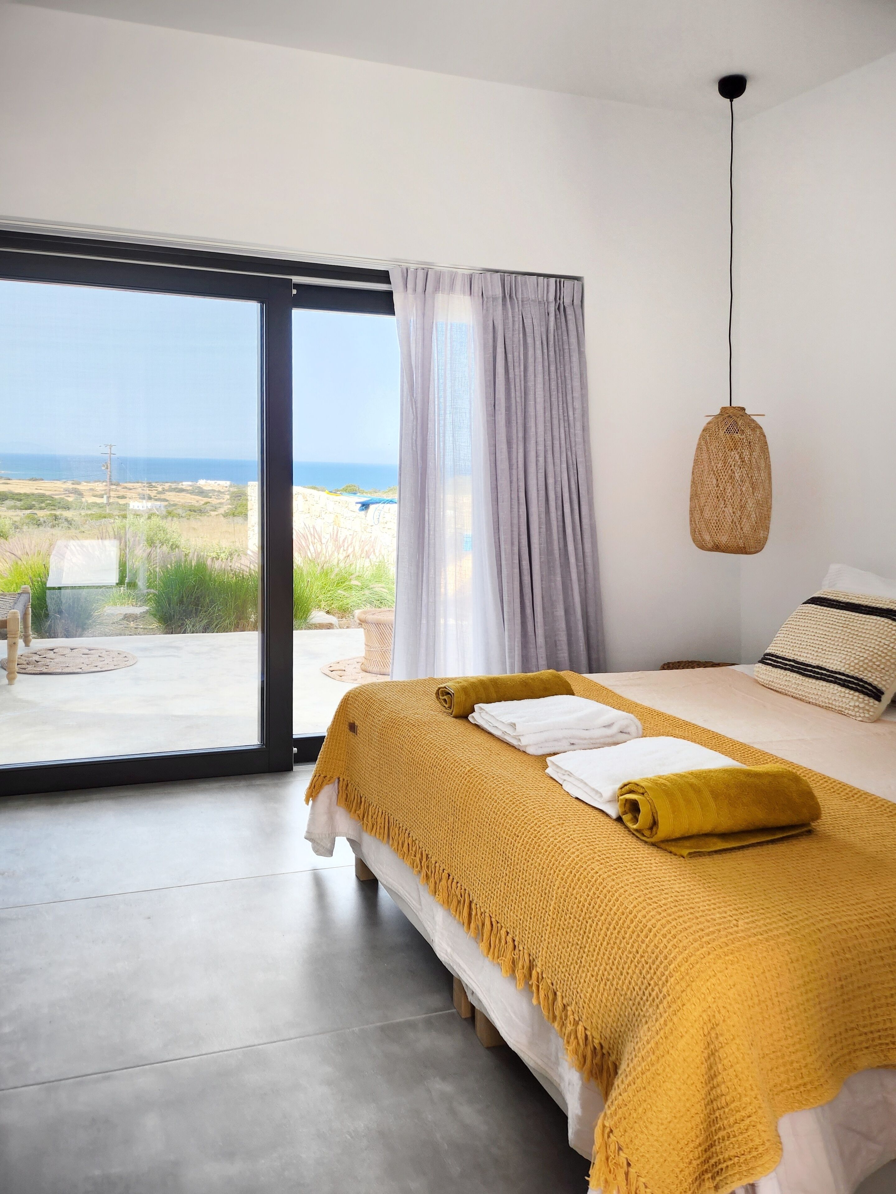 A bedroom with a bed, a view of the outdoors, and a hanging light fixture.